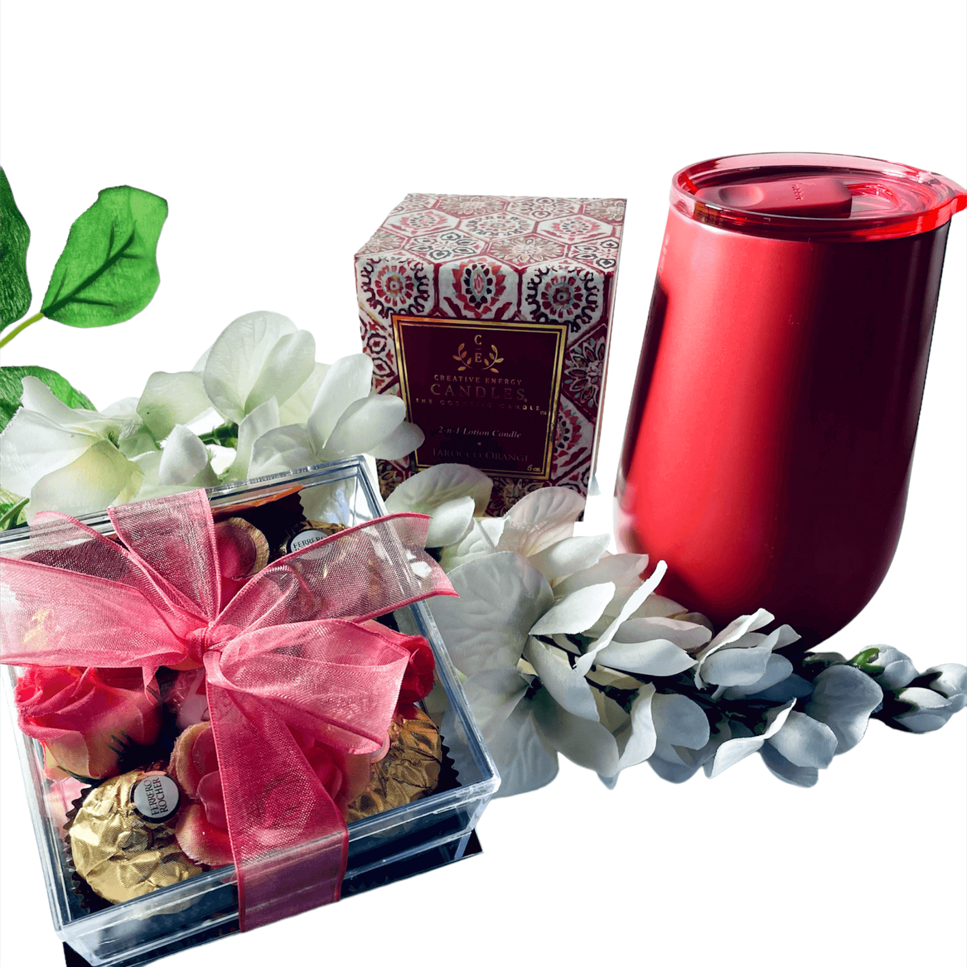 Captivating coral-toned candle and drinkware gift set surrounded by delicate white flowers and lush green leaves, creating a serene and elegant presentation.