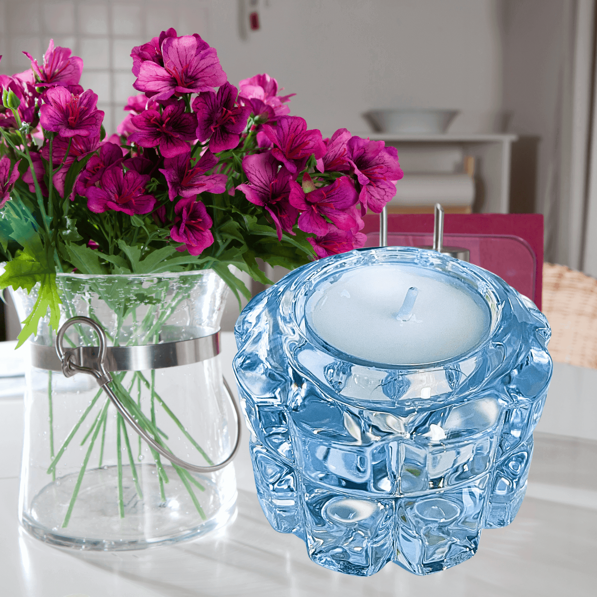 Vibrant pink petunias in a glass vase and a decorative crystal tealight holder on a table.