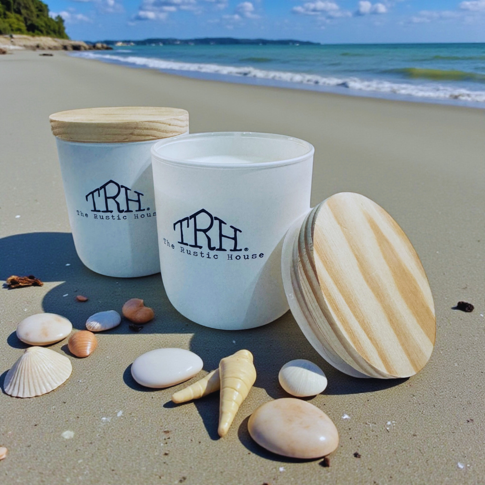 Two white containers with wooden lids on a sandy beach with seashells around them.