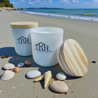 Thumbnail for Two white containers with wooden lids on a sandy beach with seashells around them.