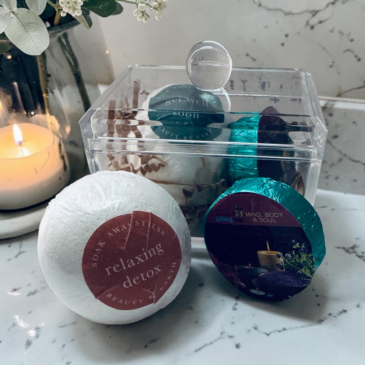 Bath bombs with decorative labels on a marble surface with a candle in the background