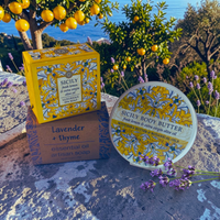 Thumbnail for Sicily Body Butter and Sicily Lavender + Thyme artisan soap products displayed outdoors on a stone surface with lemons, lavender, and a sea background. The round body butter tub and the branded yellow-and-white box are shown, along with a smaller brown box for the lavender and thyme soap.