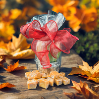 Thumbnail for Glass jar with a red bow and caramels on a wooden surface with autumn leaves.