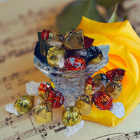 Thumbnail for Decorative glass bowl filled with gold and red wrapped candies on a yellow rose and sheet music background.