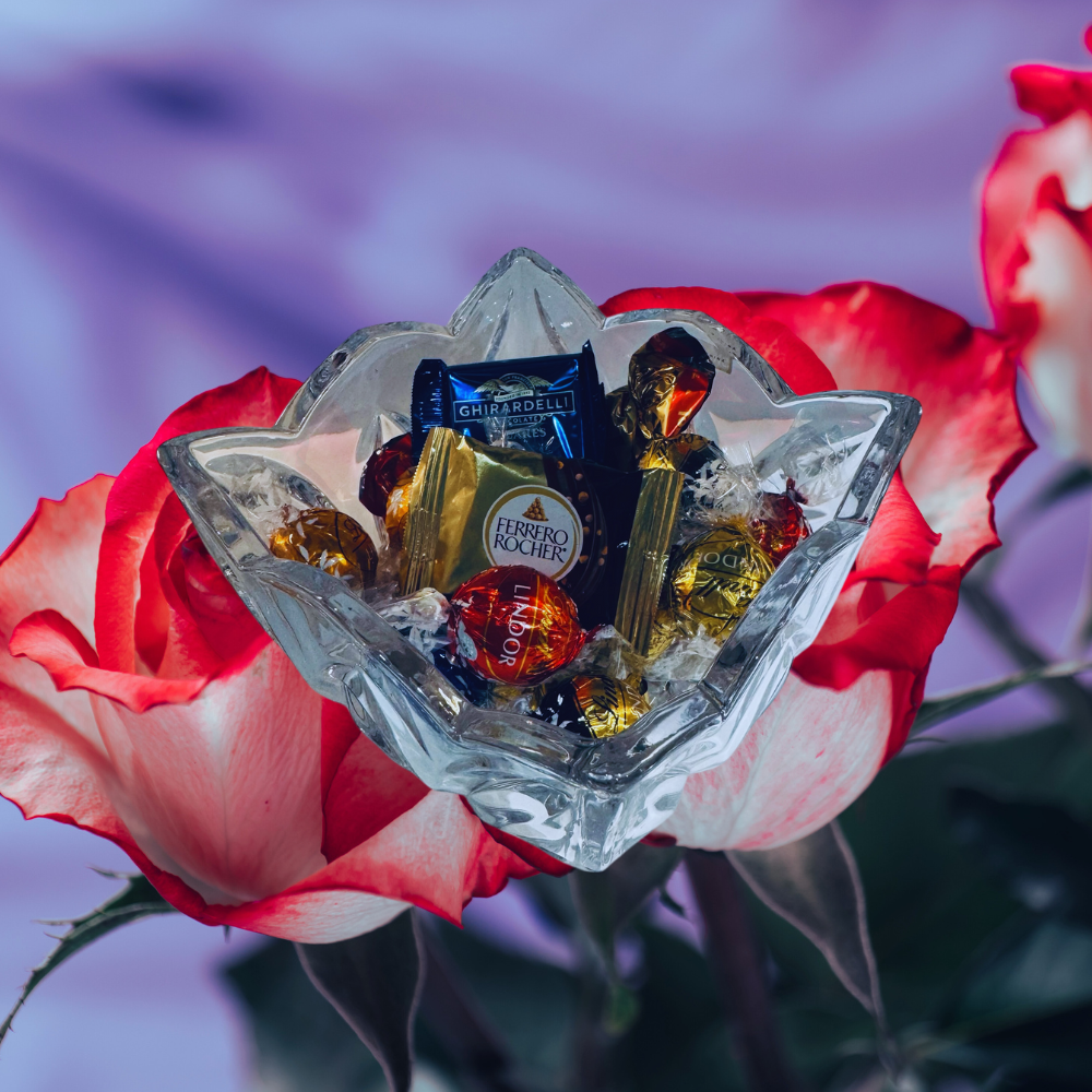 Glass bowl with chocolates on a red rose against a blurred background