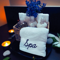 Thumbnail for Spa-themed setup with towels, bottles, and flowers on a dark surface.
