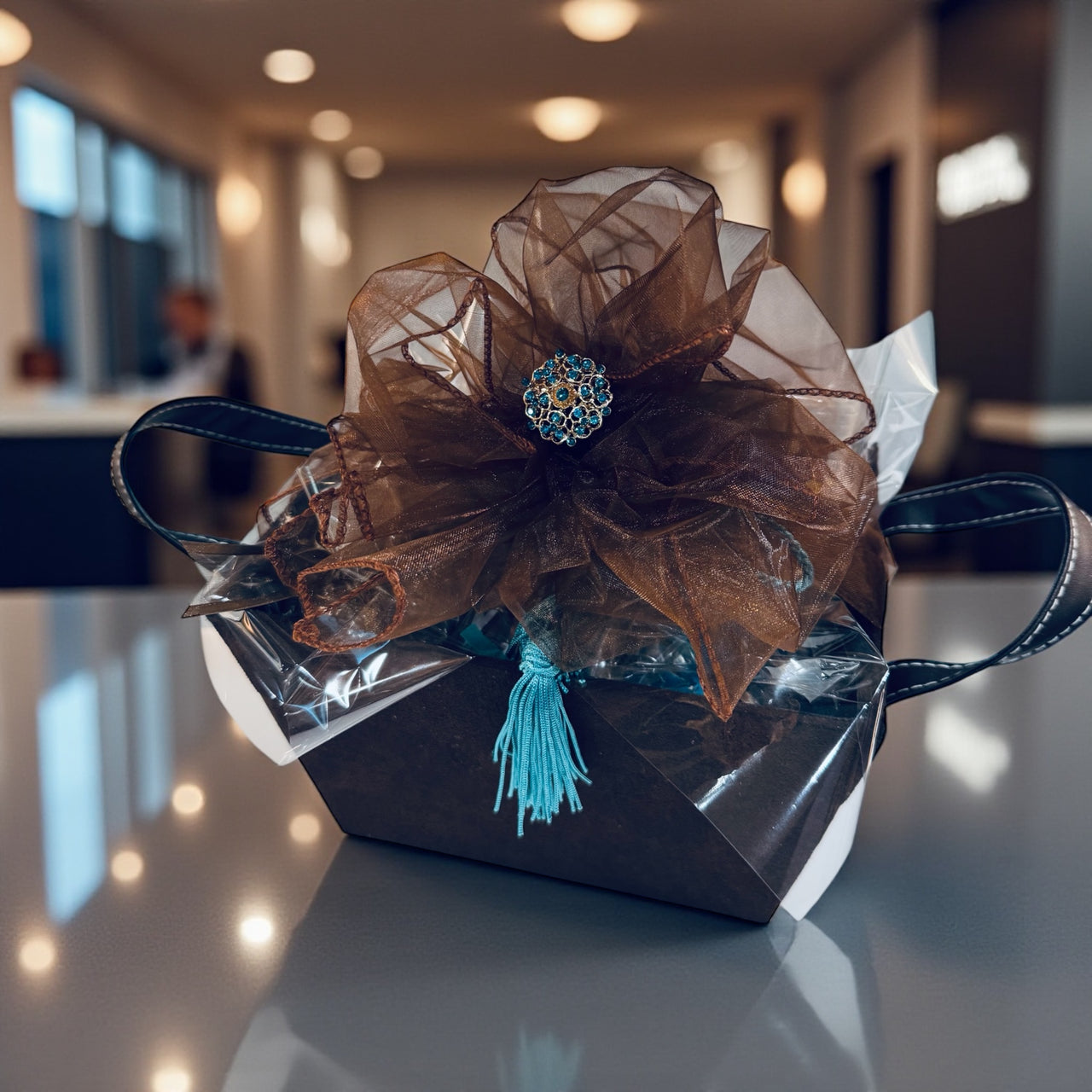 Decorative gift box with brown organza bow and blue tassel on a reflective surface.