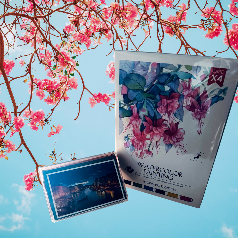 Packaging of watercolor painting paper with cherry blossoms and a scenic card against a blue sky.