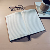 Thumbnail for Open notebook with lined pages on a wooden surface, accompanied by glasses and a mug.
