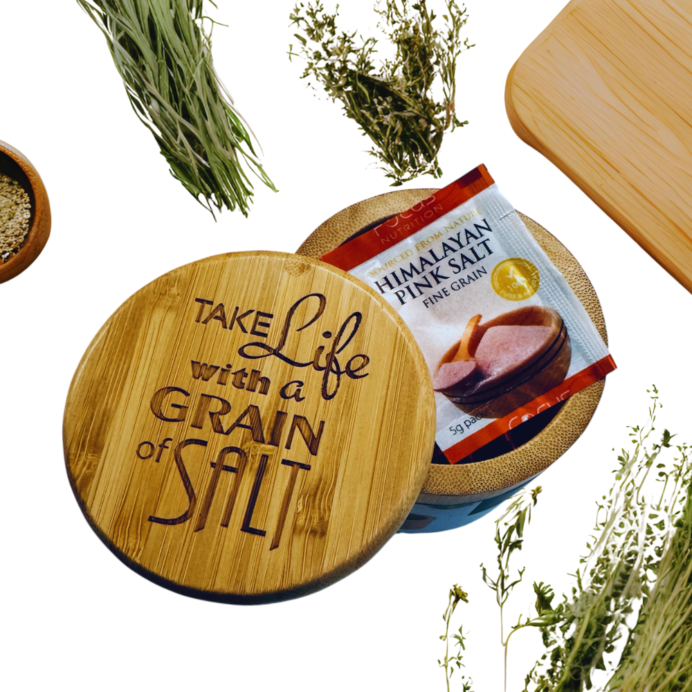 Wooden salt cellar with 'Take Life with a Grain of Salt' text, Himalayan pink salt packet, and herbs on a white background.