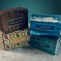 Thumbnail for Four boxed soap bars for men arranged on a light surface against a teal background. The boxes are labeled Elements Cedarwood, Elements Ocean, Elements Soap for Men, and Elements Forest, with different wood and patterned packaging designs.