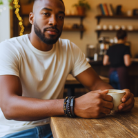 Thumbnail for Man holding a mug in a cozy cafe setting modeling bracelet