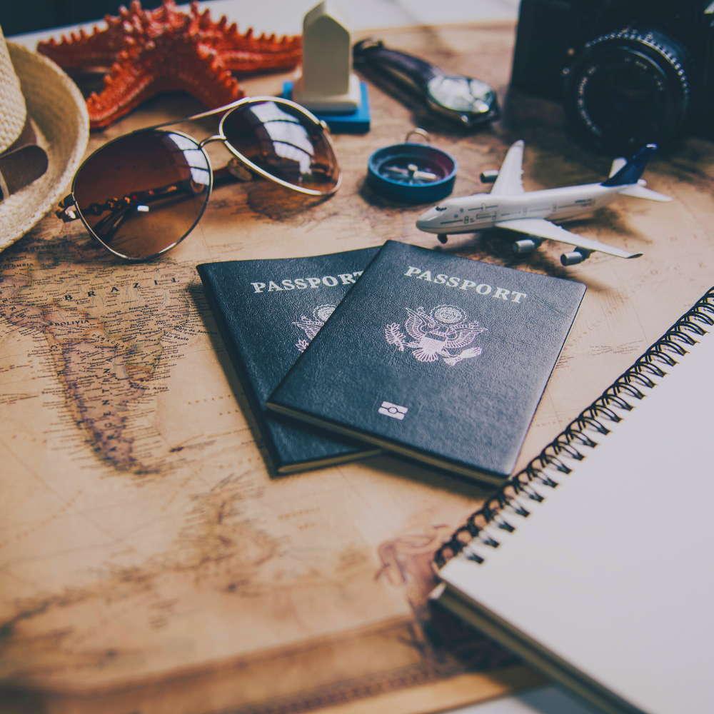Two passports on a world map with sunglasses, camera, and other travel items.