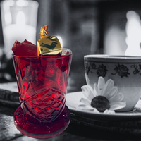 Thumbnail for Red glass with a gold cube and red leaves, next to a white teacup with black floral design on a blurred background.