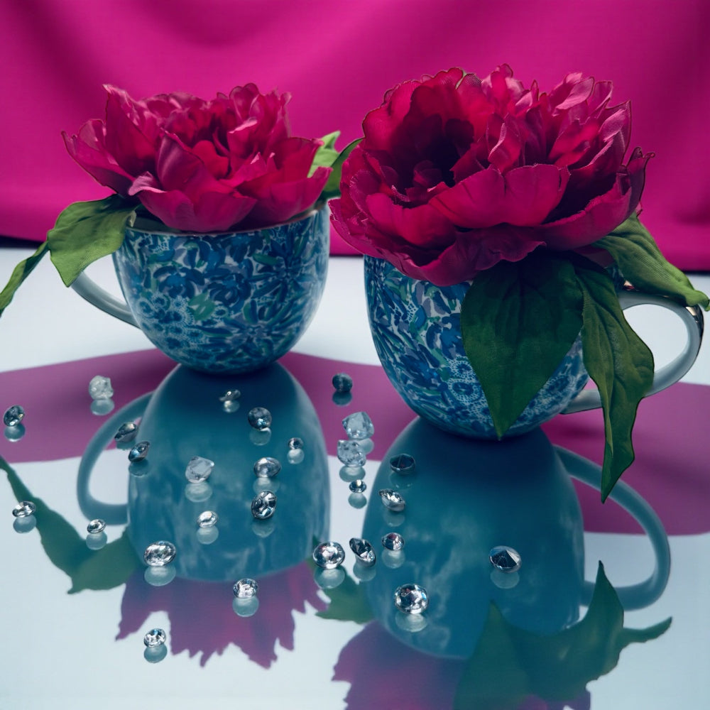 Two blue mugs with pink flowers on a reflective surface with a pink background