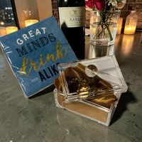 Thumbnail for Decorative box with gold interior, blue card with 'Great Minds Drink Aliki' text, and wine bottle on a table.