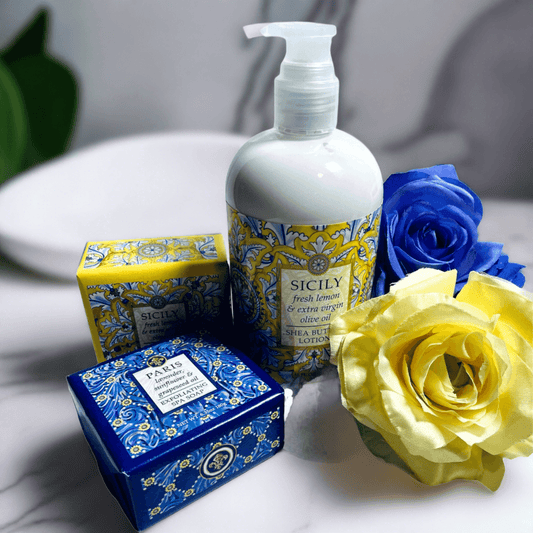 Elegant bath and body products featuring the Sicily Collection from Essentialgifting.com. The image showcases a bottle of lotion, a decorative box, and vibrant yellow and blue flowers, creating a luxurious, Mediterranean-inspired display.